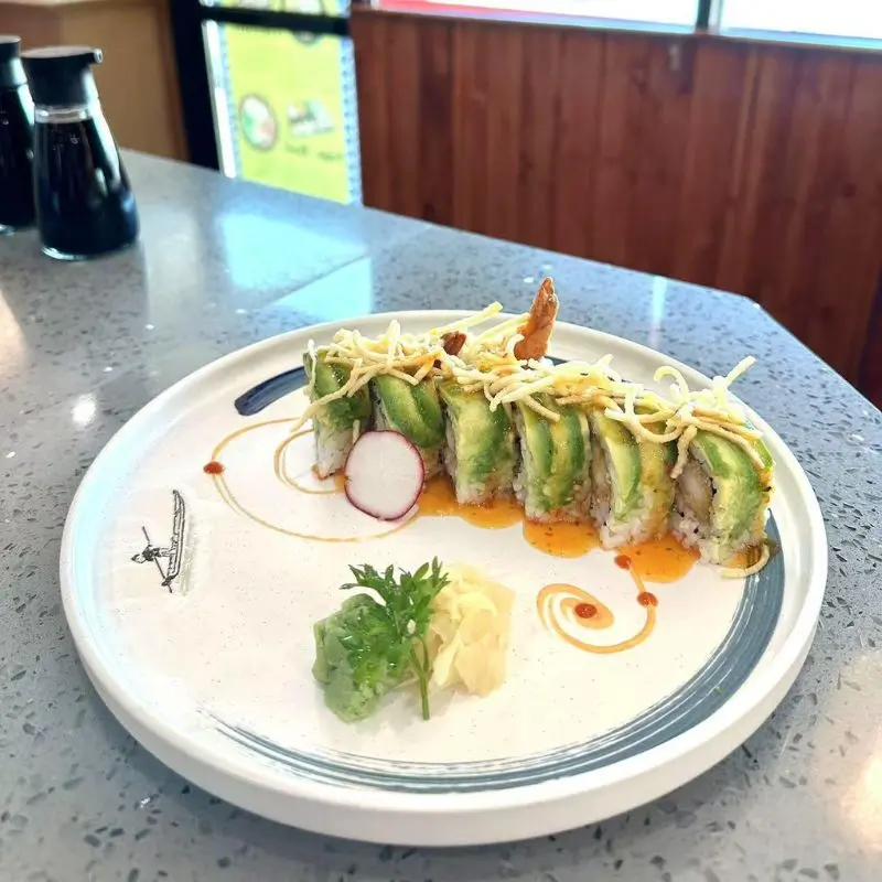 Sushi roll topped with avocado, shrimp, and fried noodles, decorated neatly.