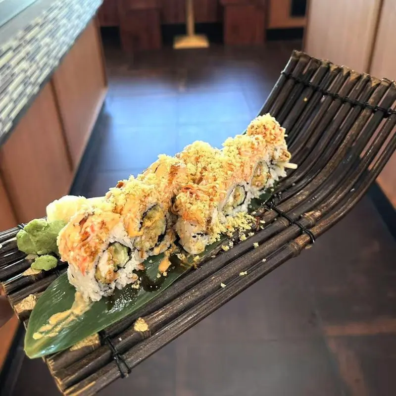 Sushi roll topped with crispy bits, served on a bamboo - like tray.