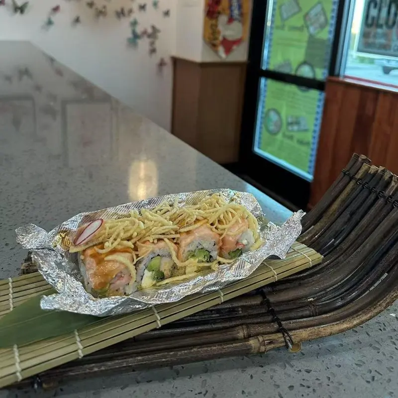 Sushi roll garnished with fried noodles, wrapped in aluminum foil.